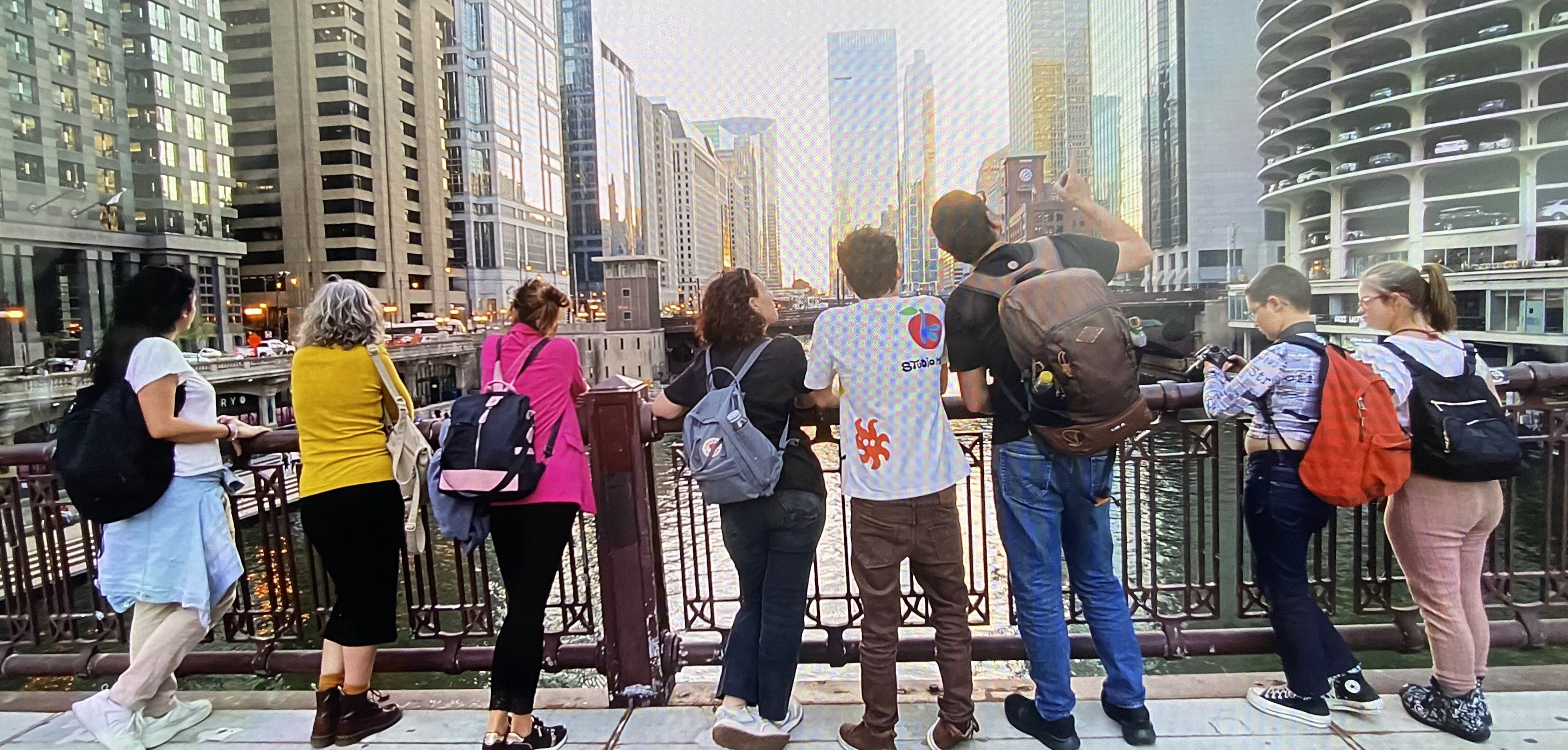 Un grupo de personas aparece de espaldas sobre un puente de Chicago mirando hacia arriba rodeados de rascacielos