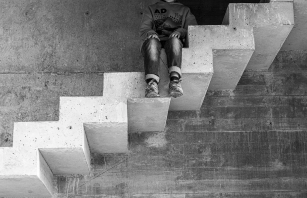 Imagen en blanco y negro de unas escaleras de cemento sin barandilla. En una de las escaleras superiores se ven las piernas colgando de un niño que está allí sentado. Sólo se ve la imagen del niño del cuello para abajo.