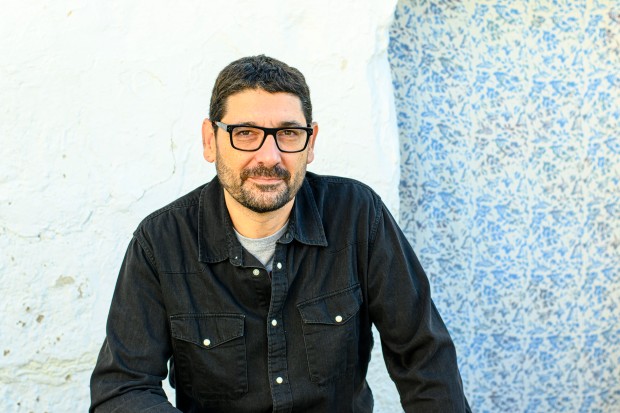 Retrato de Nacho Calderón realizado por Paula Verde Francisco. Aparece de cintura para arriba, vestido de negro y con el fondo blanco de una pared encalada.
