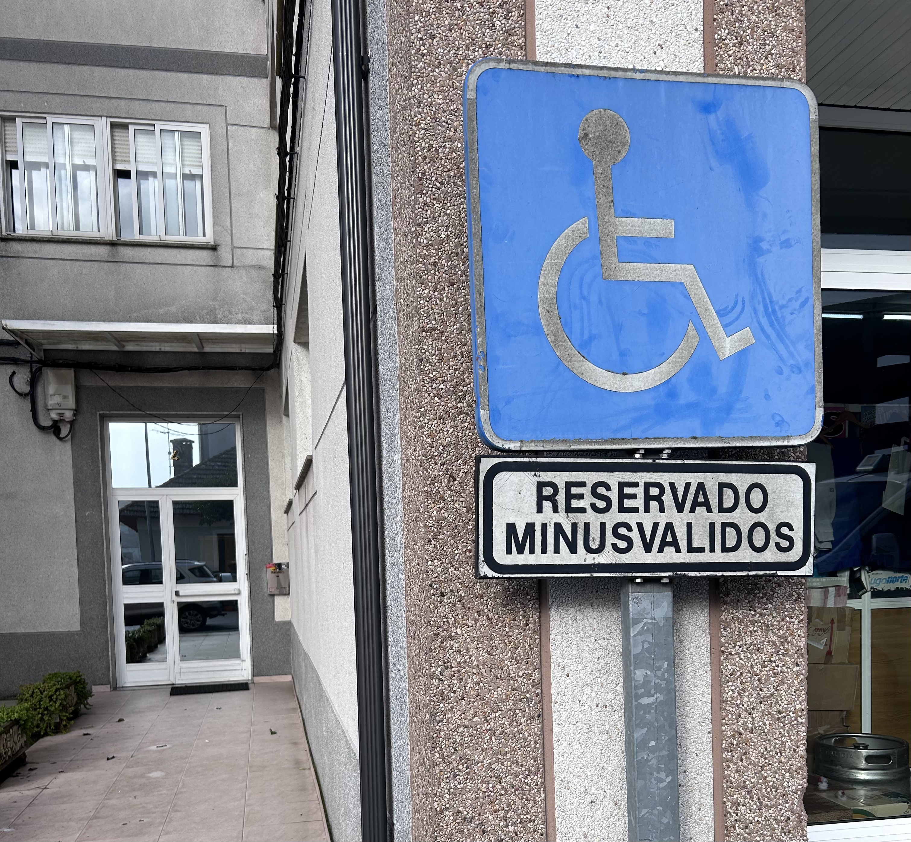 Señal vertical que identifica una plaza de aparcamiento accesible. Bajo el icono internacional de accesibilidad aparece una placa donde puede leerse: “RESERVADO MINUSVÁLIDOS”.